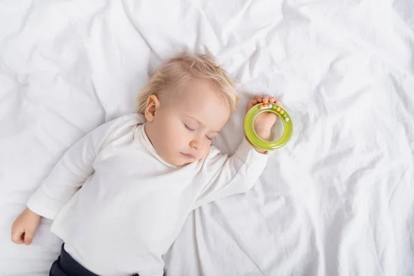 Top view of toddler sleeping with rattle on white bedding at home — Stock Photo