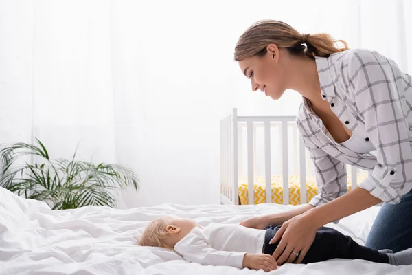 Seitenansicht einer jungen Frau, die sich im Schlafzimmer über ihren kleinen Sohn beugt — Stockfoto