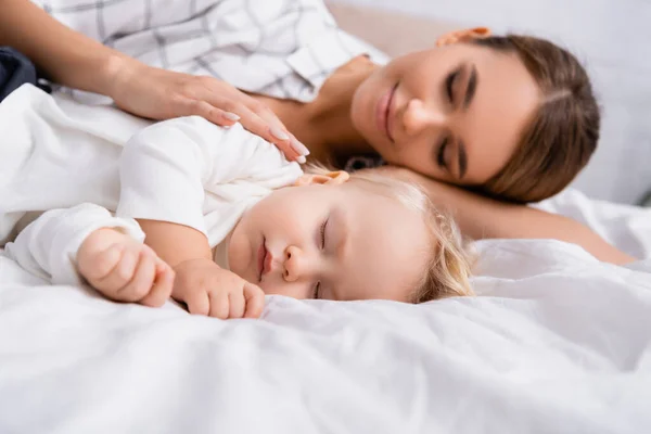 Surface level of happy woman with closed eyes touching sleeping son, blurred background — Stock Photo