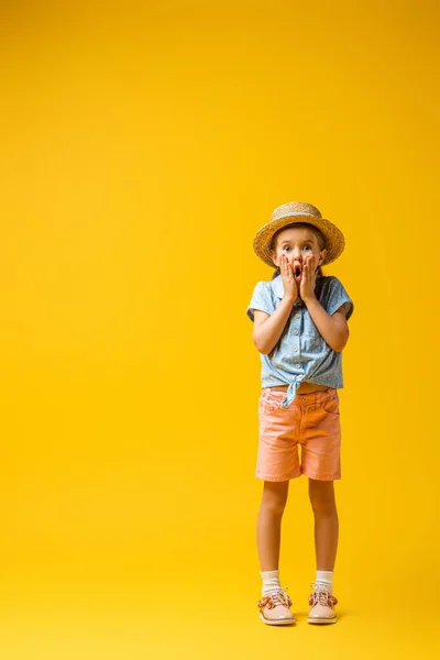 Comprimento total do garoto chocado em chapéu de palha olhando para a câmera no amarelo — Fotografia de Stock