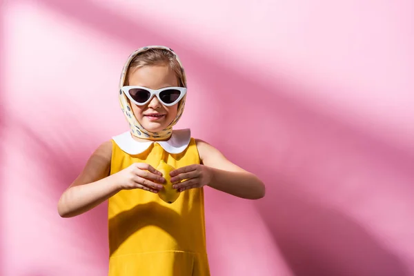 Chica sonriente en pañuelo para la cabeza y gafas de sol con limón fresco en rosa - foto de stock