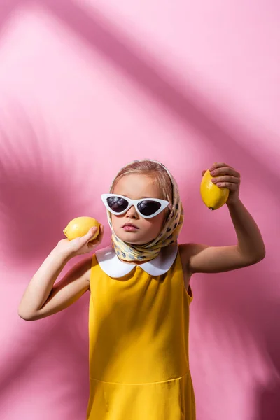 Chica con estilo en el pañuelo para la cabeza y gafas de sol con limones frescos en rosa - foto de stock