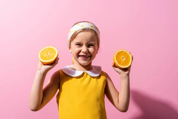 Happy girl in headscarf holding orange halves on pink — Stock Photo