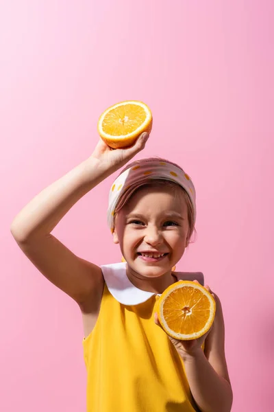 Sonriente chica en la cabeza bufanda celebración de naranja mitades en rosa - foto de stock