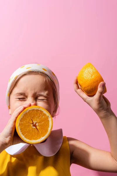 Girl with closed eyes covering mouth with orange half isolated on pink — Stock Photo