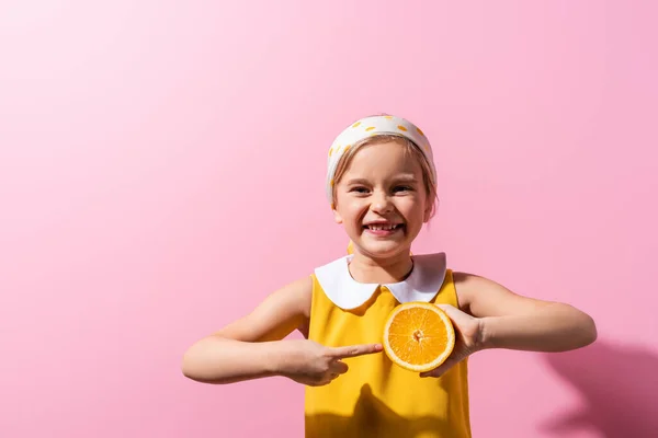 Chica positiva señalando con el dedo a la mitad naranja en rosa - foto de stock