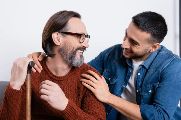 Smiling hispanic man hugging shoulders of happy father at home — Stock Photo