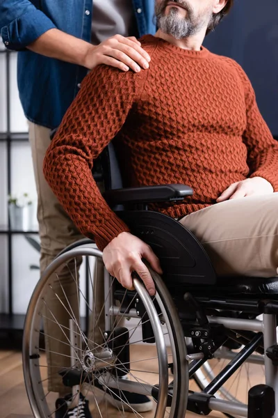 Vista parcial del hombre tocando el hombro del padre discapacitado en silla de ruedas - foto de stock