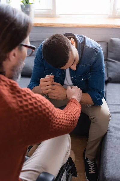 Handicapped man calming frustrated hispanic son sitting with bowed head, blurred foreground — Stock Photo