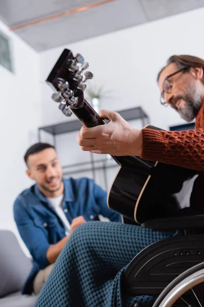 Vista de ángulo bajo del hombre discapacitado tocando la guitarra cerca de su hijo hispano sobre fondo borroso - foto de stock