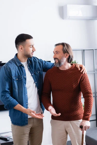 Joven hispano abrazando feliz padre mientras habla en casa - foto de stock