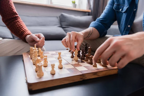 Обрезанный вид отца и сына, играющих в шахматы дома, размытый передний план — стоковое фото