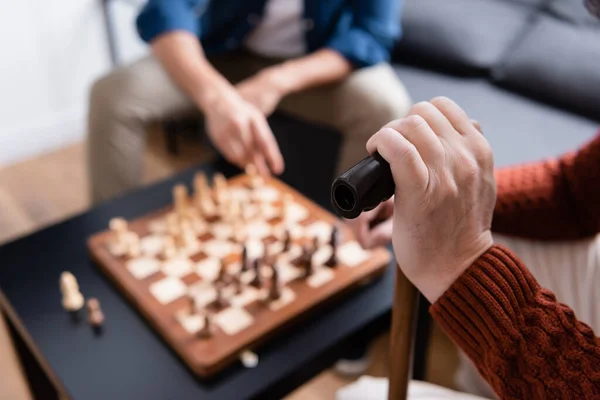 Partial view of man with walking stick playing chess with son on blurred background — Stock Photo