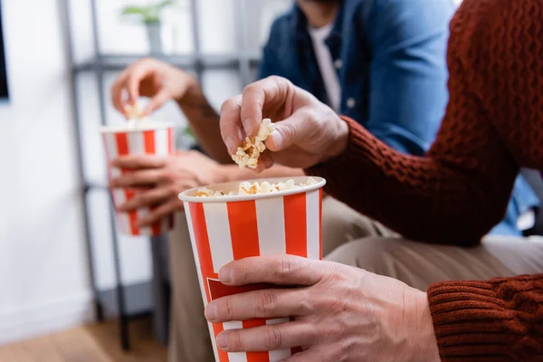 Vista recortada de padre e hijo comiendo palomitas de maíz en casa, fondo borroso - foto de stock