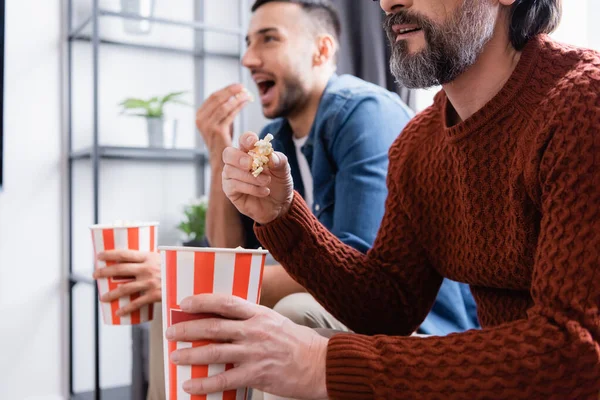 Interracial padre e hijo viendo tv mientras comer palomitas de maíz en casa, fondo borroso - foto de stock