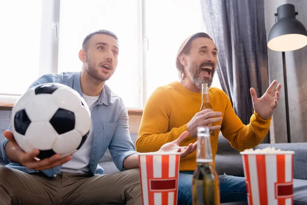 Amazed interracial father and son watching football championship near beer and popcorn on blurred foreground — Stock Photo