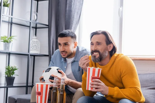 Worried interracial dad and son watching soccer championship with beer and popcorn at home — Stock Photo