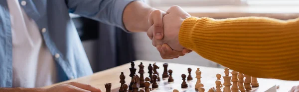Cropped view of father and son shaking hands near chessboard on blurred background, banner — Stock Photo
