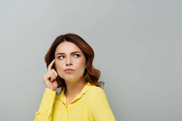 Thoughtful woman with curly hair looking away while touching head with finger isolated on grey — Stock Photo