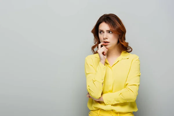 Angespannte Frau denkt, während sie die Lippe mit dem Finger berührt und wegschaut auf grau — Stockfoto