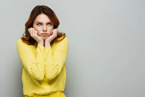 Donna offesa guardando in alto mentre si tiene le mani vicino al viso sul grigio — Foto stock