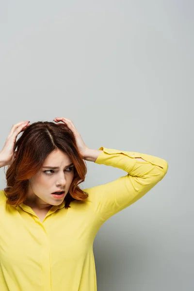 Mujer tensa con el pelo rizado tocando la cabeza mientras mira hacia otro lado en gris - foto de stock