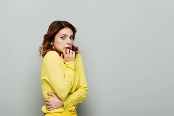 Tense woman holding hand near mouth while looking at camera on grey — Stock Photo