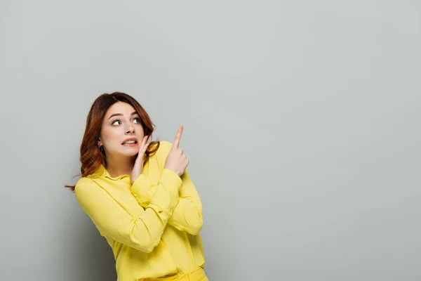 Scared woman in yellow blouse looking away and pointing with finger on grey — Stock Photo