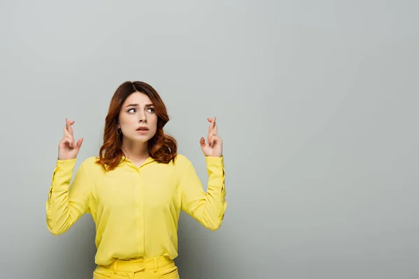 Worried woman standing with crossed fingers and looking away on grey — Stock Photo