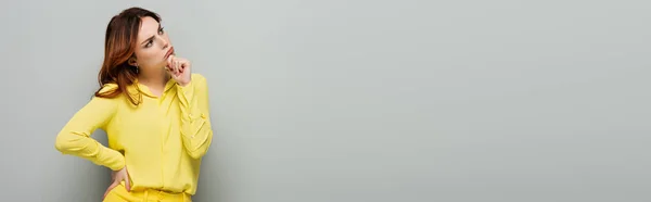Thoughtful woman standing with hand on hip and looking away on grey, banner — Stock Photo