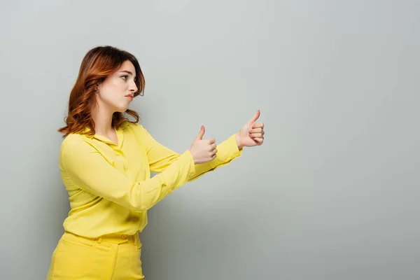 Jealous woman looking away and showing thumbs up on grey — Stock Photo