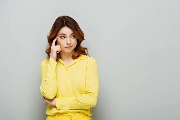 Pensive woman touching head with finger while looking away on grey — Stock Photo