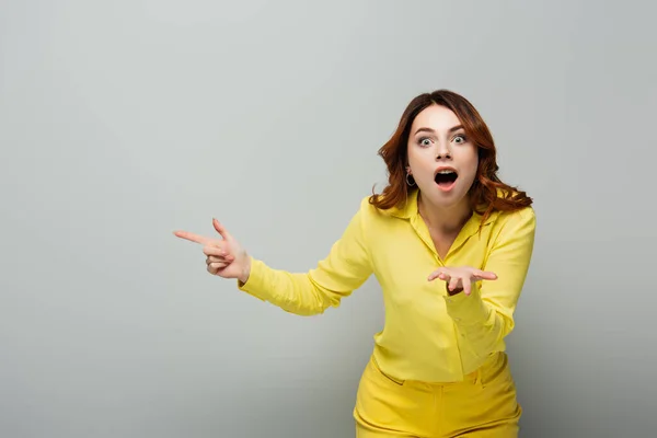 Amazed woman pointing with hand and finger while looking at camera on grey — Stock Photo