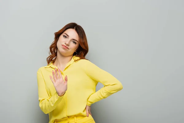 Mujer disgustada mostrando gesto de rechazo mientras está de pie con la mano en la cadera en gris - foto de stock