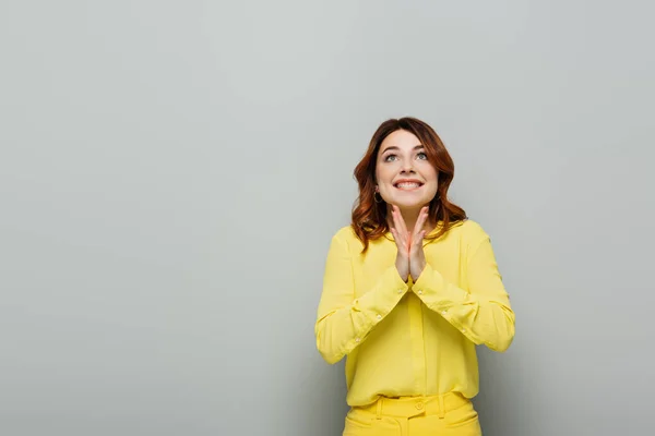 Joyful woman in yellow shirt looking up and clapping hands on grey — Stock Photo