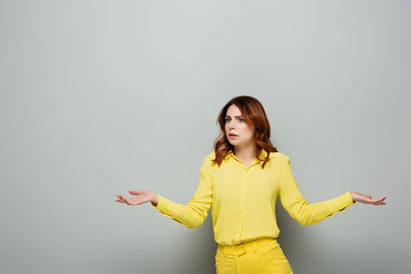 Amazed woman looking away while showing shrug gesture on grey — Stock Photo