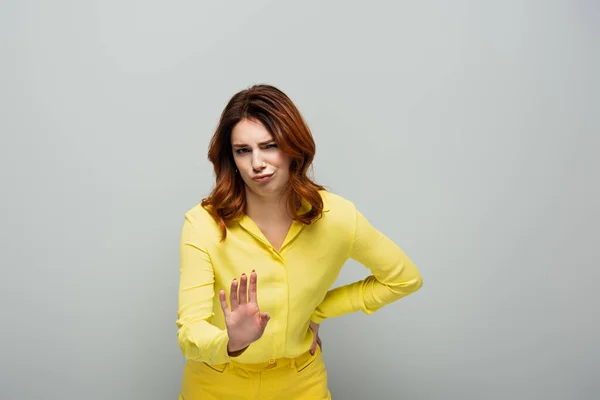 Displeased woman looking at camera while showing stop gesture on grey — Stock Photo