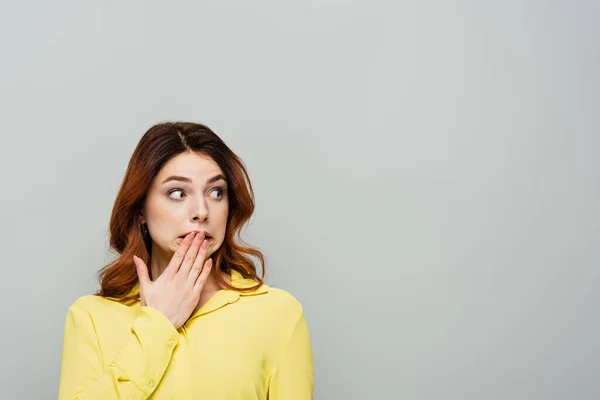 Schockierte Frau bedeckt Mund mit der Hand, während sie isoliert auf grau wegschaut — Stockfoto