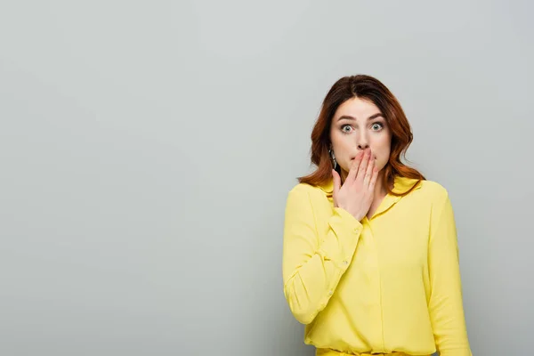 Thrilled woman in yellow blouse covering mouth with hand on grey — Stock Photo