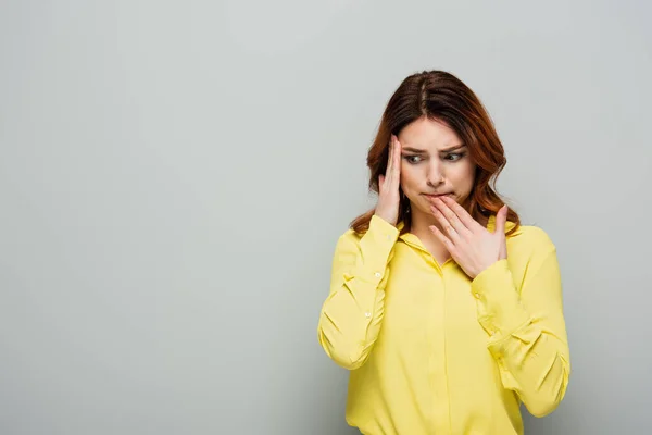 Worried woman in yellow shirt touching head while standing on grey — Stock Photo