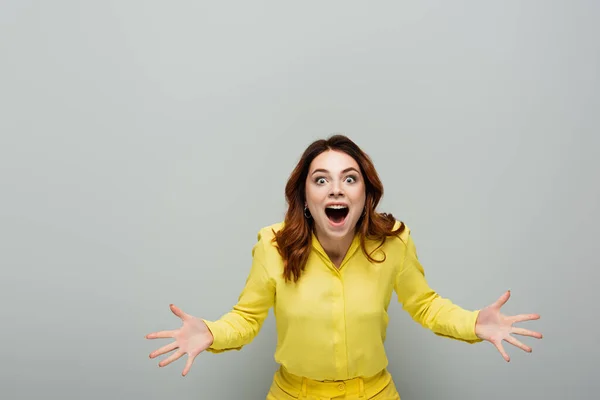 Amazed woman looking at camera while standing with open arms on grey — Stock Photo