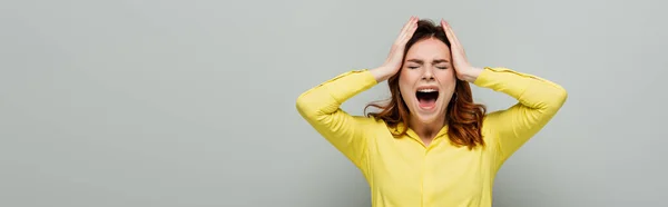 Angry woman screaming while standing with closed eyes and touching head on grey, banner — Stock Photo