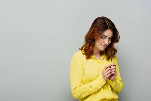 Femme rusée en chemise jaune souriant tout en regardant la caméra sur gris — Photo de stock