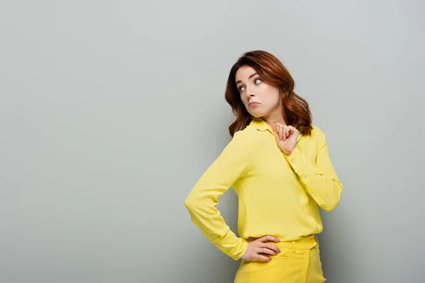 Femme découragée regardant loin tout en se tenant avec la main sur la hanche sur gris — Photo de stock