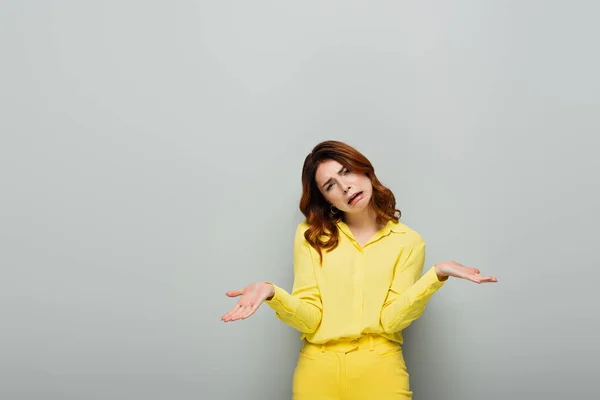 Upset woman showing shrug gesture while looking at camera on grey — Stock Photo