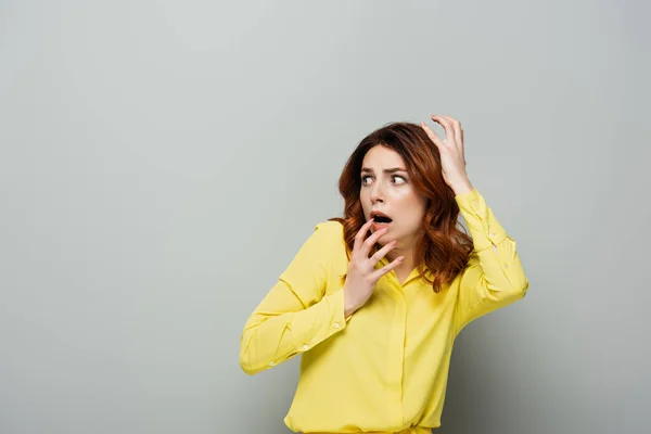 Mulher assustada na camisa amarela gesticulando enquanto olha para o cinza — Fotografia de Stock