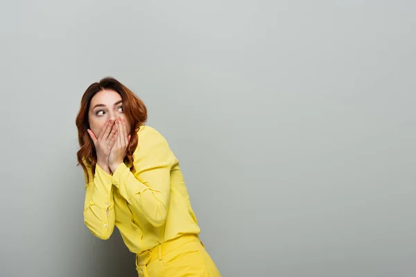 Scared woman in yellow clothes covering mouth while looking away on grey — Stock Photo