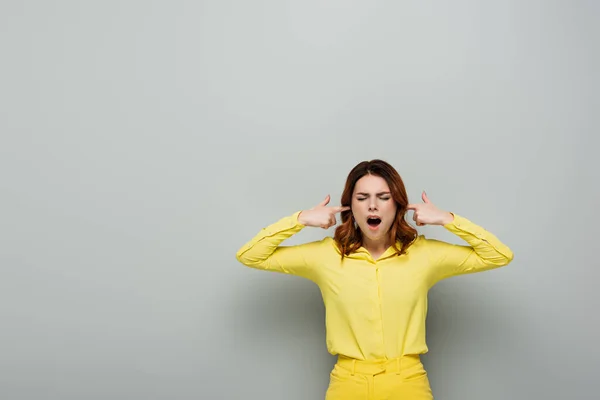 Donna irritata tappando le orecchie mentre in piedi con gli occhi chiusi sul grigio — Foto stock