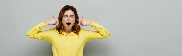 Mulher irritada gritando enquanto tapava os ouvidos em cinza, banner — Fotografia de Stock