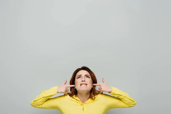 Dissatisfied woman looking up while plugging ears on grey — Stock Photo